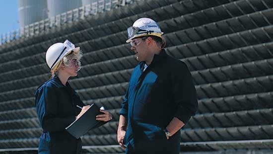 Two Ecolab experts in hardhats conversating on site in an outdoor industrial area. 