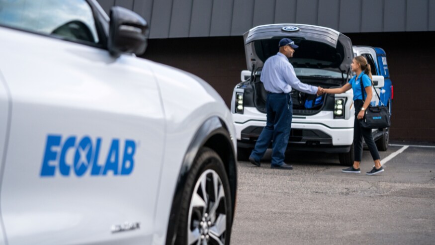 Ford and Ecolab associates shaking hands.  Ecolab vehicles, Ford brand, in the front and in the background. . 