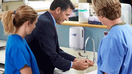Business man demonstrating Ecolab Hand Hygiene Products for hospital professionals over a sink.